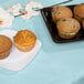 A table with a Pastel Blue Tissue Table Cover with plates of muffins on it.