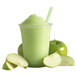 A green smoothie in a cup with a straw and green apple slices.