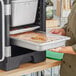 A woman holding a Vollrath stainless steel transport pan full of food.