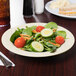 A plate of salad with tomatoes, cucumbers, carrots, and a sandwich.