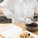 A person using a Vollrath Ivory Perforated Oval Spoodle to serve pasta with sauce.