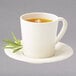 An ivory melamine mug filled with tea on a saucer with a leaf on it.