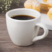 An ivory espresso cup filled with coffee on a table with pastries.