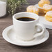 An ivory espresso cup of coffee on a plate next to some pastries.