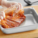 A gloved hand using a plastic bag to put red sauce in a Full Size steam table pan.