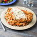 A Diamond Ivory melamine plate with cheese and pasta, chicken, salad, and tomatoes on a table.