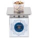 An Edlund Four Star portion scale with a plastic container of nuts and seeds on top.