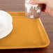 A person holding a cup over a rectangular Tuscan gold Cambro tray.