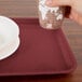 A hand holding a cup over a Cambro tray with a plate on it.