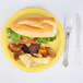 A Creative Converting Mimosa yellow paper plate with a sandwich and potato chips.