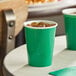 Two emerald green Creative Converting paper hot cups with ice and drinks on a table.