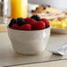 A bowl of raspberries and blackberries with a fork on a table.