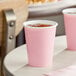 A stack of pink Creative Converting paper cups with a pink cup filled with water.