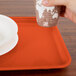 A person holding a paper cup and a plate on an orange rectangular tray.