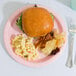 A plate of Classic Pink paper dinnerware with a hamburger and macaroni.