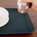 A hand holding a cup over a Cambro rectangular slate blue fiberglass tray.