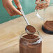 A hand using a Tablecraft stainless steel measuring scoop to pour coffee into a jar.