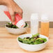 A hand using a Tablecraft Invertatop squeeze bottle to pour pink liquid onto a bowl of salad.