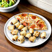 A Fiesta white china pizza tray with a pepperoni pizza and sausage rolls.