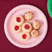 A table with a Classic Pink Creative Converting paper plate holding a coconut cookie.