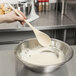 A person mixing white liquid in a bowl with a Thunder Group wooden spoon.