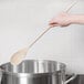 A hand holding a Thunder Group wooden spoon over a pot.