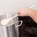 A hand holding a Thunder Group wooden spoon over a pot of water.