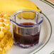 A table with a glass cup of syrup next to a waffle and a GET Syrup and Cream Mini Pitcher.