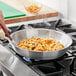 A person cooking food in a Choice aluminum fry pan on a stove.