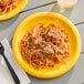 A Creative Converting School Bus Yellow paper plate with spaghetti and meatballs on it.