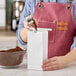 A woman using a silver tin tie to pour coffee into a white paper bag.