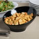 A black slanted melamine bowl filled with croutons next to a salad.