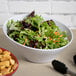 A white Elite Global Solutions melamine bowl filled with salad on a table next to a bowl of croutons.