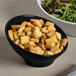 An Elite Global Solutions black slanted melamine bowl filled with salad and croutons.