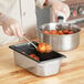 A person stirring meatballs in a Vollrath stainless steel steam table pan.