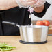 A person cooking food in a Vollrath stainless steel sauce pan with a black silicone handle.