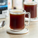 A glass mug of Crown Beverages Emperor's Blend espresso on a wooden coaster.
