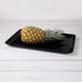 A pineapple on a black rectangular melamine tray.