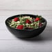 A black Elite Global Solutions round melamine bowl filled with salad and strawberries.