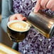 A person pouring Crown Beverages Emperor's Blend whole bean espresso into a cup of coffee.