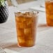 A clear 12 oz. hard plastic tumbler filled with iced tea and ice cubes.