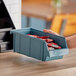 A hand holding a blue Cambro Versa organizer bin full of red packets.