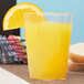 A Fineline clear hard plastic tumbler filled with orange juice with a slice of orange on top.