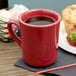 A red Tuxton Tiara mug on a table with a drink next to a muffin.