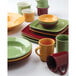 A variety of Tuxton Tiara mugs in red, yellow, and green on a table.