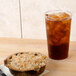 A clear plastic tumbler filled with ice tea on a table with a pie.