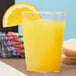 A Fineline clear plastic tumbler filled with orange juice with a slice of orange on the rim.