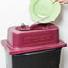 A person using a San Jamar KatchAll Flatware Retriever to collect a fork from a black trash can with a red edge.