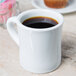 A CAC Hartford white porcelain mug filled with brown liquid on a table.