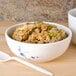 A blue Thunder Group Blue Bamboo melamine bowl filled with rice next to a white spoon on a white table.